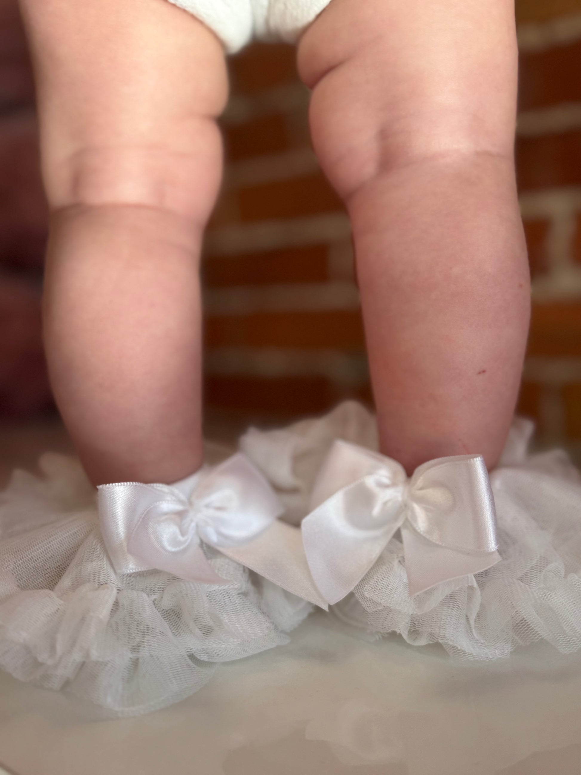 White lace garter with bows worn by a child, against a blurred brick wall background.