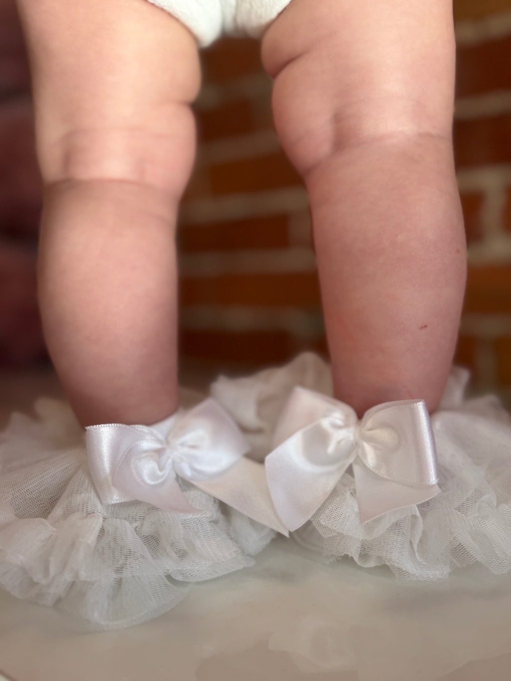 White lace garter with bows worn by a child, against a blurred brick wall background.