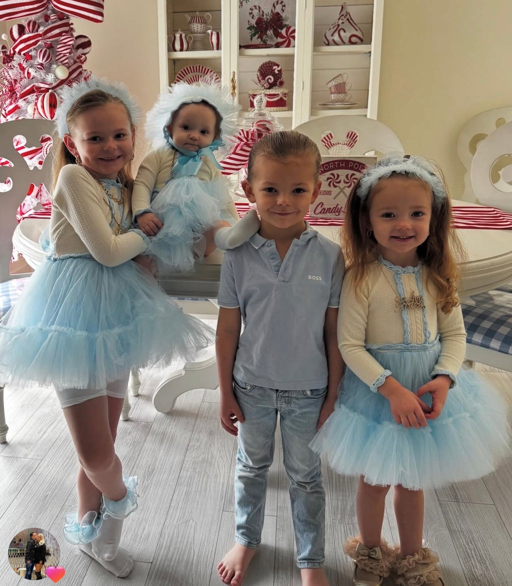 Three children in matching outfits with a doll in a room decorated for Christmas.