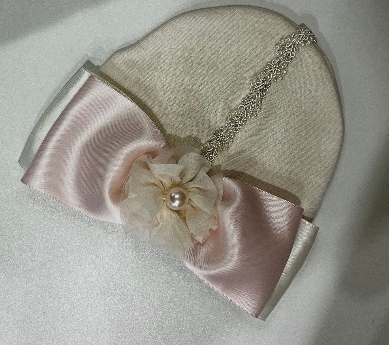 Beige and pink headband with decorative flower and pearl on a light background