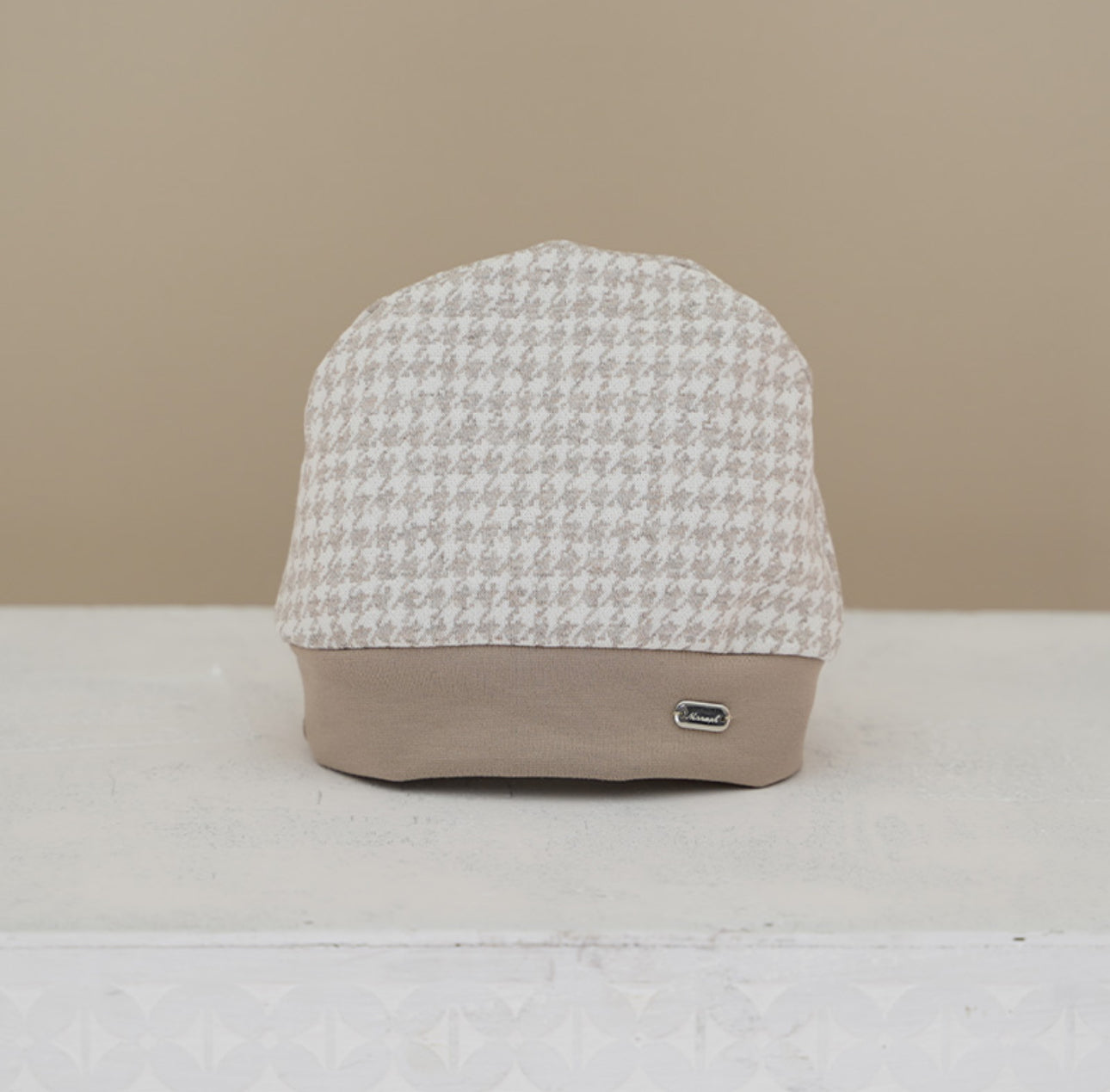Soft brushed cotton houndstooth baby cap in beige &amp; cream. Matches Dino Collection outfits, hats, booties &amp; coats. Sizes 0–12M.