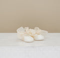 Pair of white baby shoes with ruffles on a light background