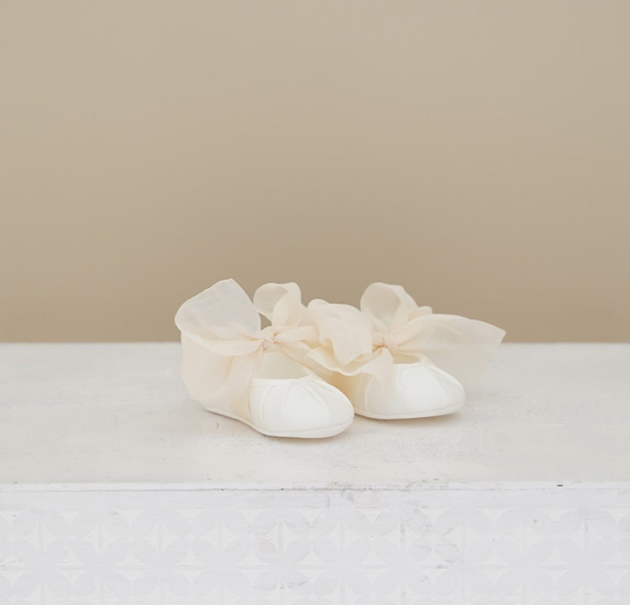 Pair of white baby shoes with ruffles on a light background