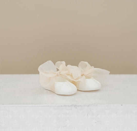 Pair of white baby shoes with ruffles on a light background