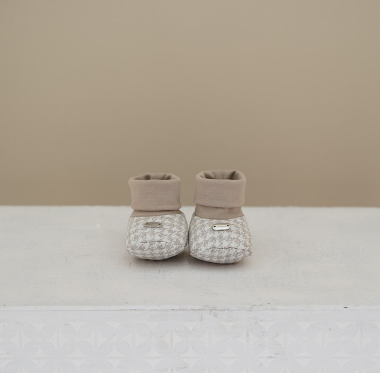 Soft brushed cotton baby booties in beige &amp; cream houndstooth. Matches outfits, hats, and coats from the Dino Collection. Sizes 3–12M.